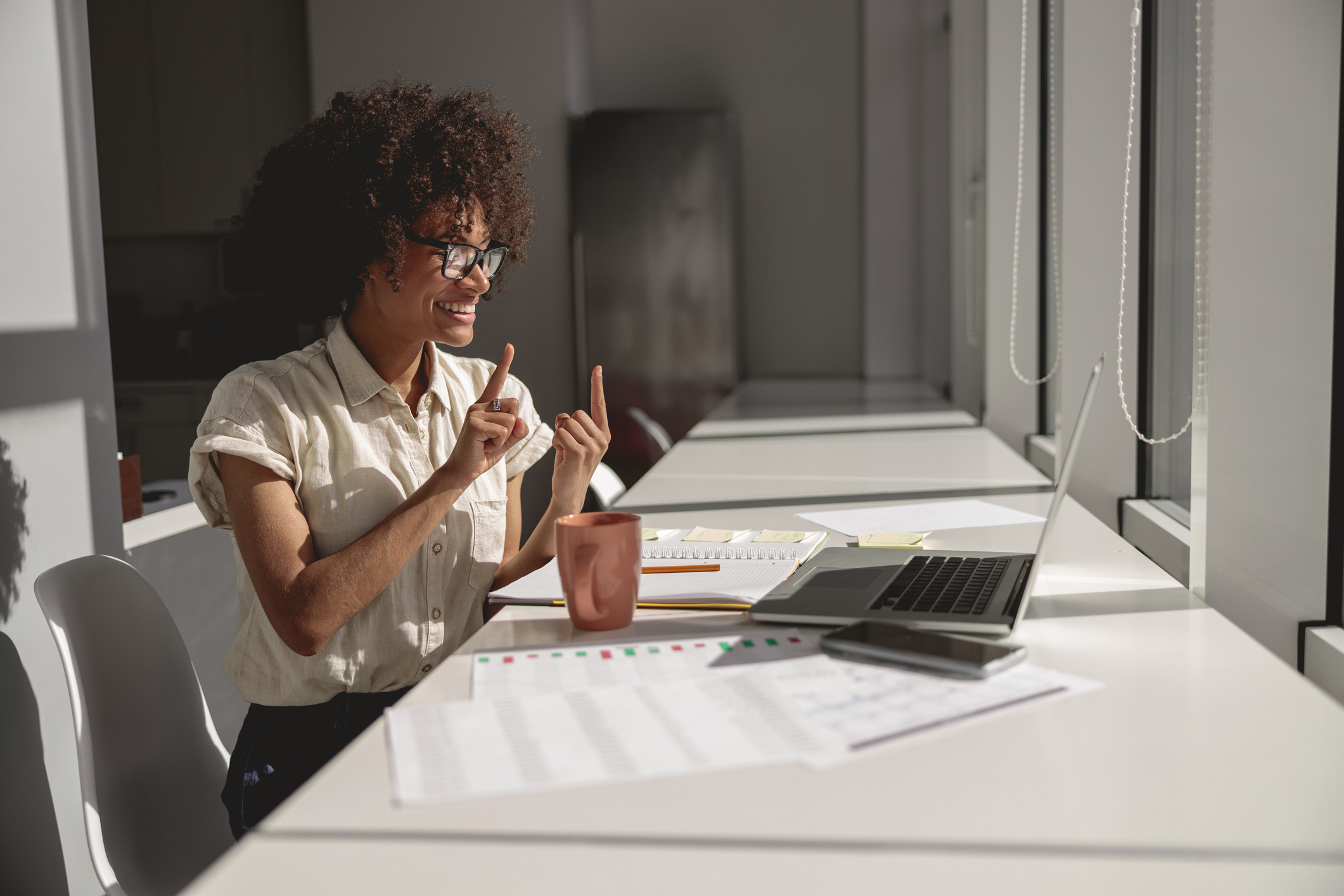 A young Black woman uses sign language online on a laptop while sitting in an office