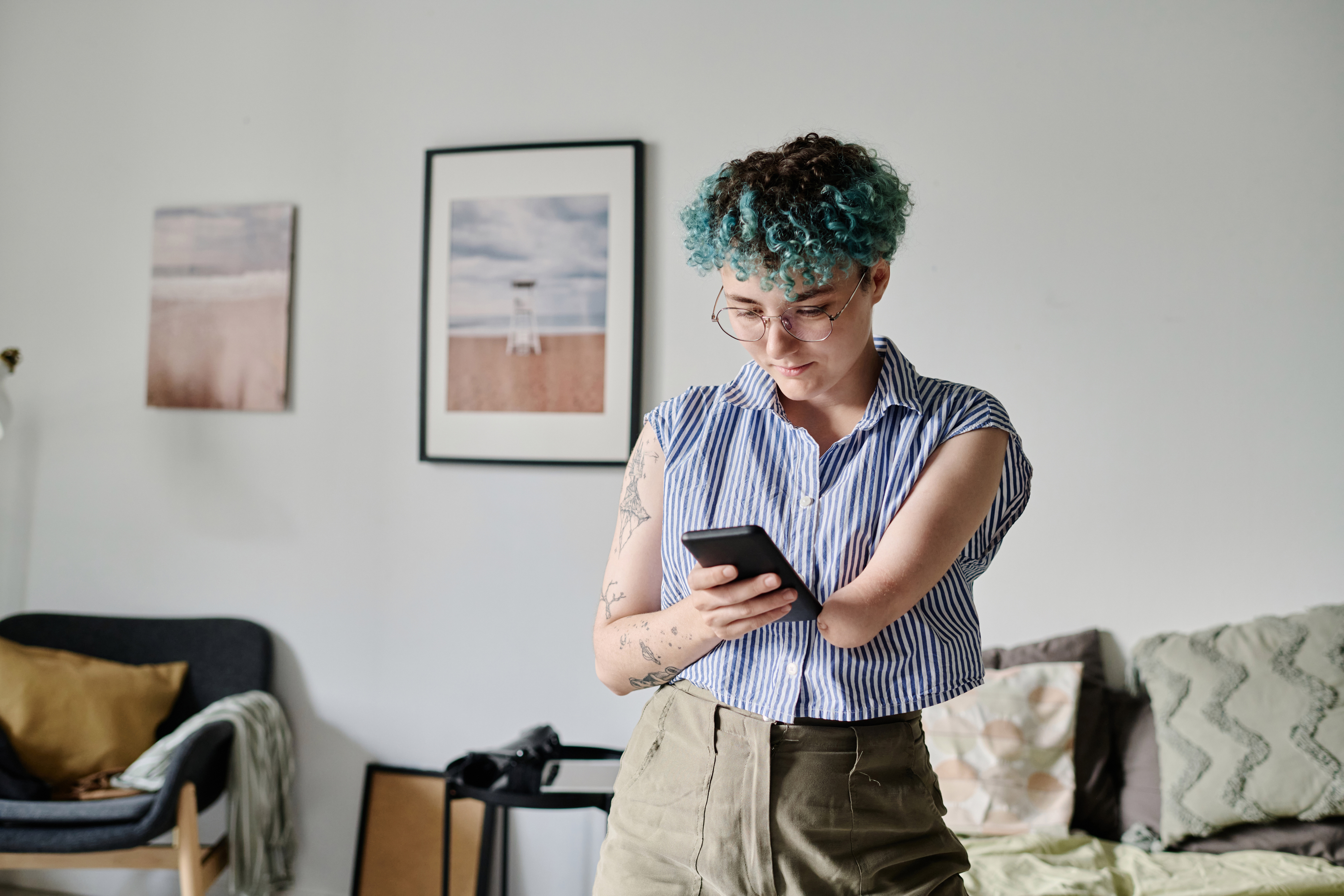 Woman with amputated arm stands in a living room and uses a smartphone