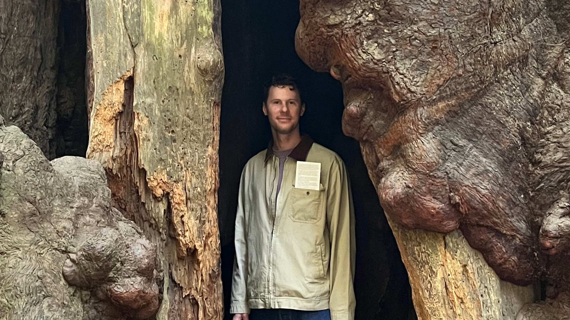 Grant Smith standing at the foot of a tree wearing jeans.